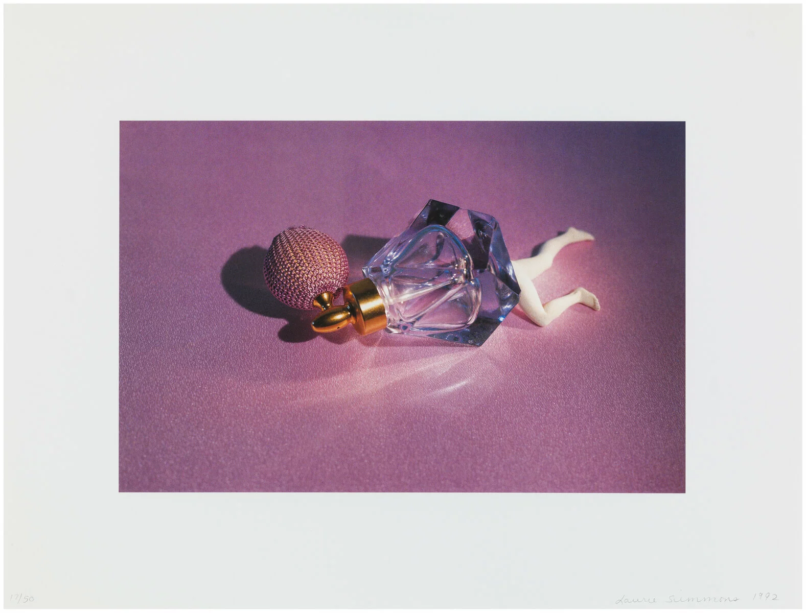 An old-fashioned perfume bottle laying on its side against a pink backdrop with bare human legs coming out from the bottom of the bottle.