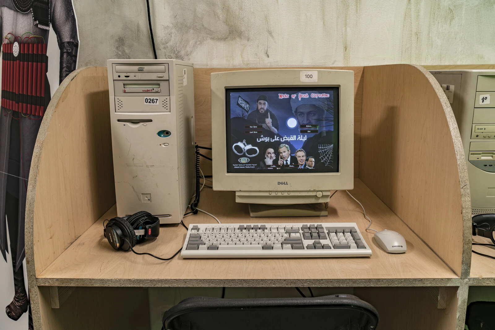 An old desktop computer on a plywood desk with dividers. The computer screen displays an old-looking video game on it