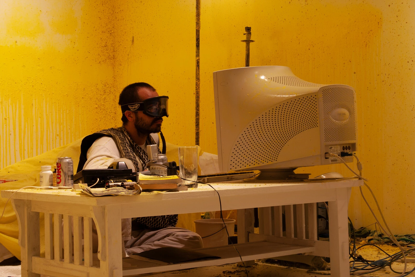 A man in ski goggles sits at a computer in a yellow room.