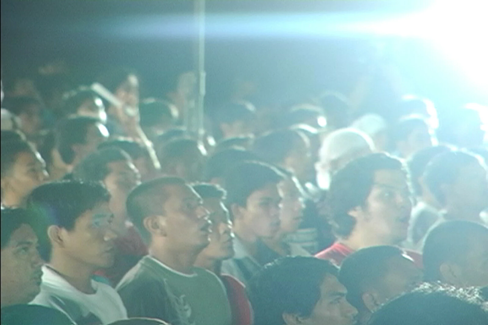 A crowd of men cast in a haze from a bright light above them