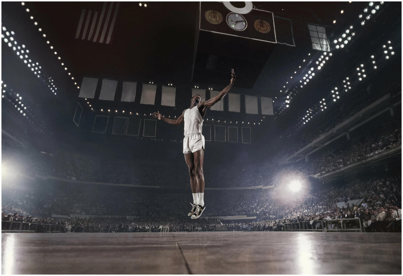 a basketball player hovering above our line of sight in a cruciform position in an arena filled with spectators