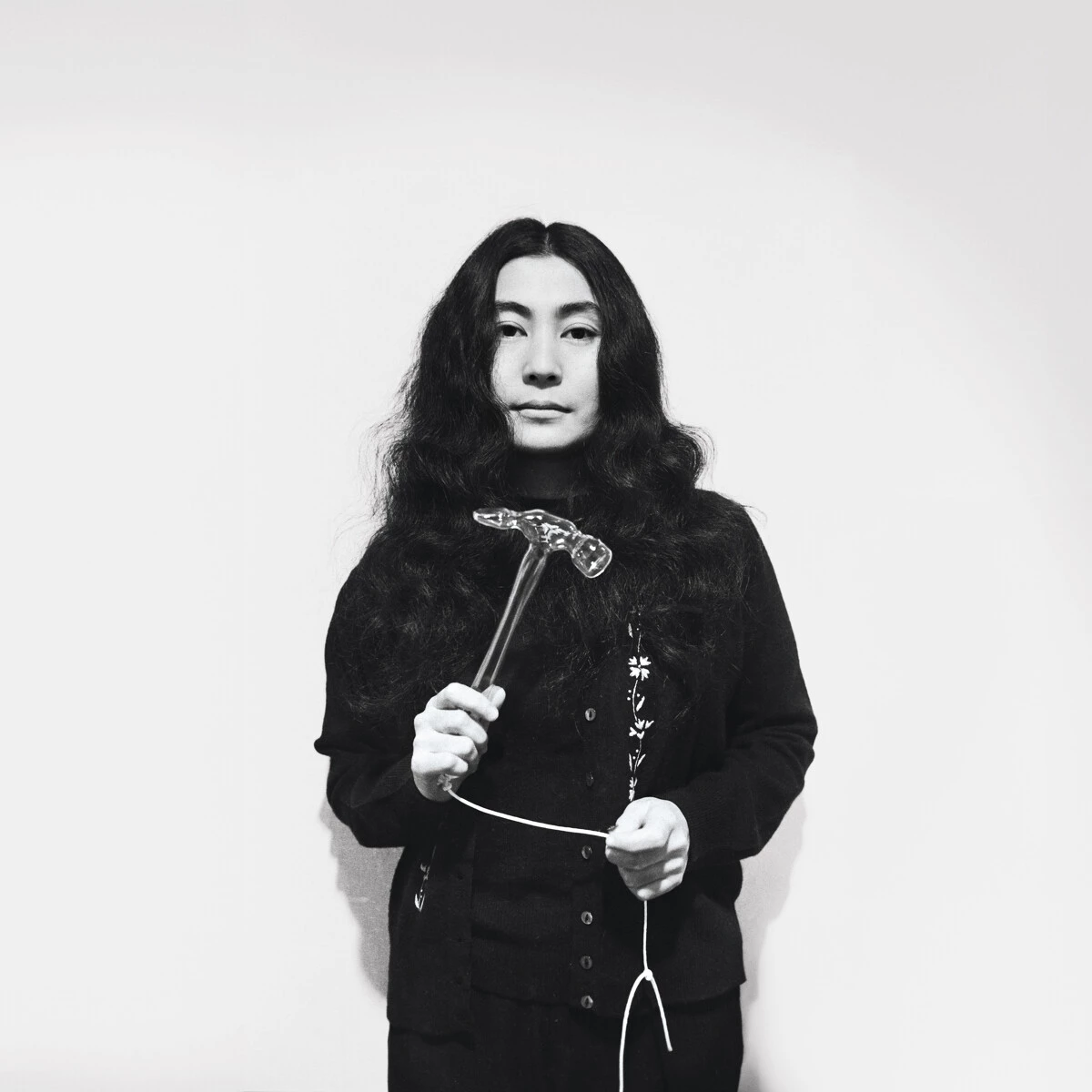 Black and white archival photo of Yoko Ono holding a hammer attached to a string