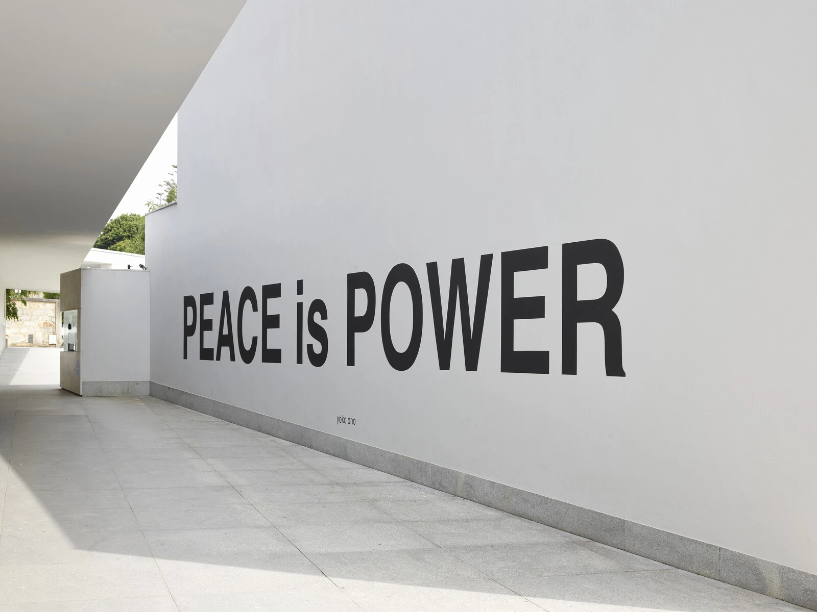 View down a long outdoor hallway with large black text on a white wall reading Peace is Power