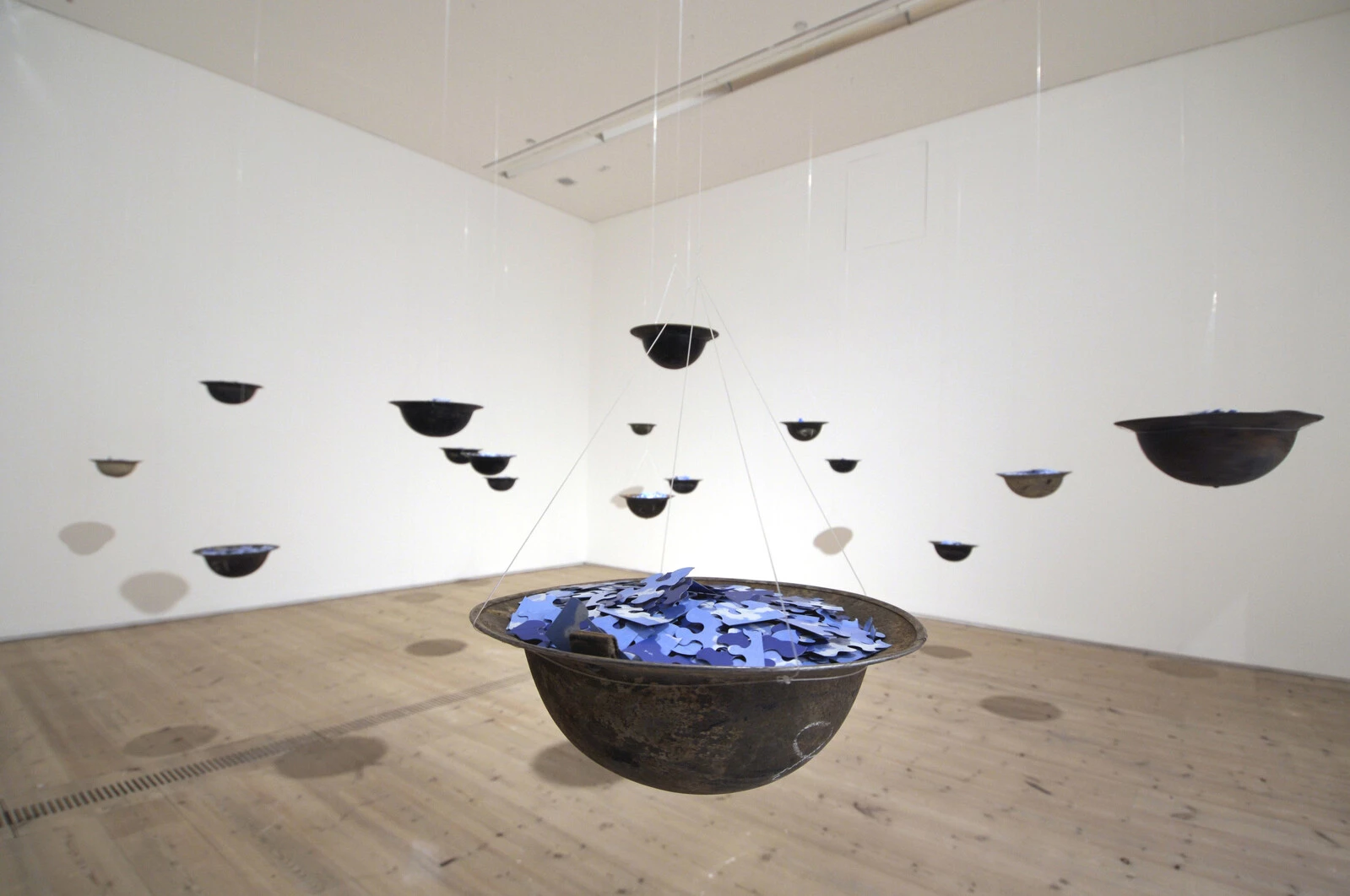 Installation of hanging bowls filled with blue puzzle pieces in a white walled gallery space
