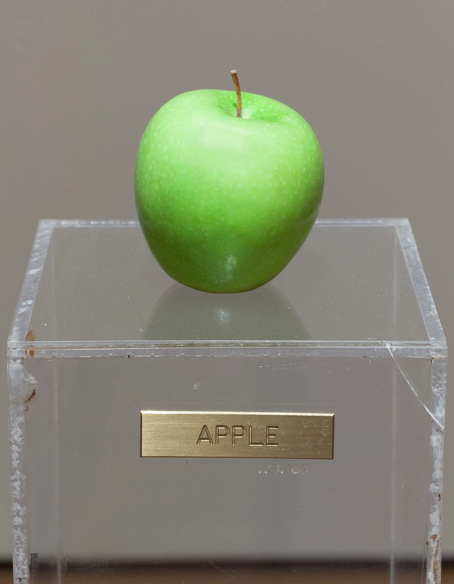 A green apple on a plexiglas pedestal with a gold plaque reading Apple