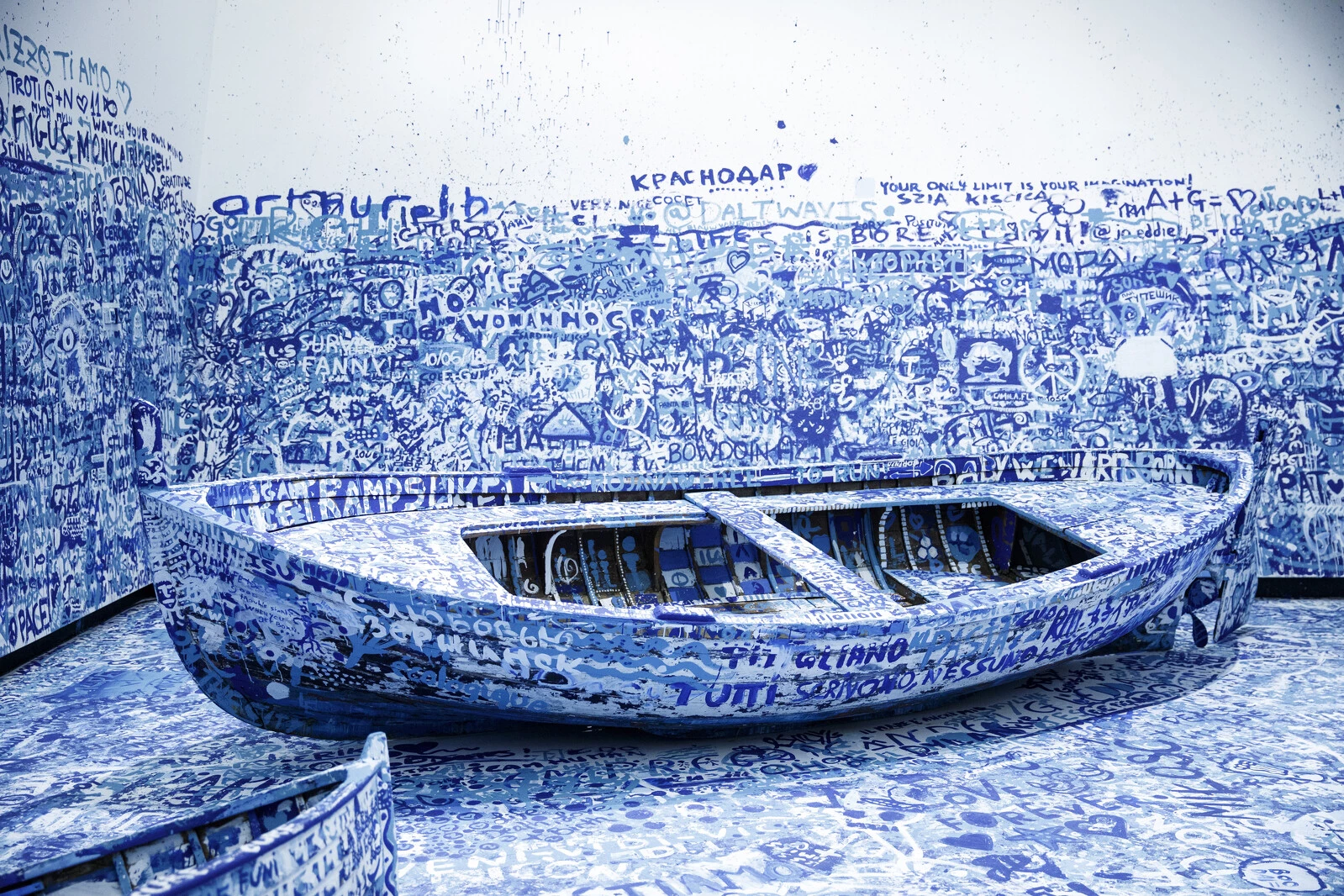 A boat in a white walled room covered in blue writing, including on the walls and floor surrounding it