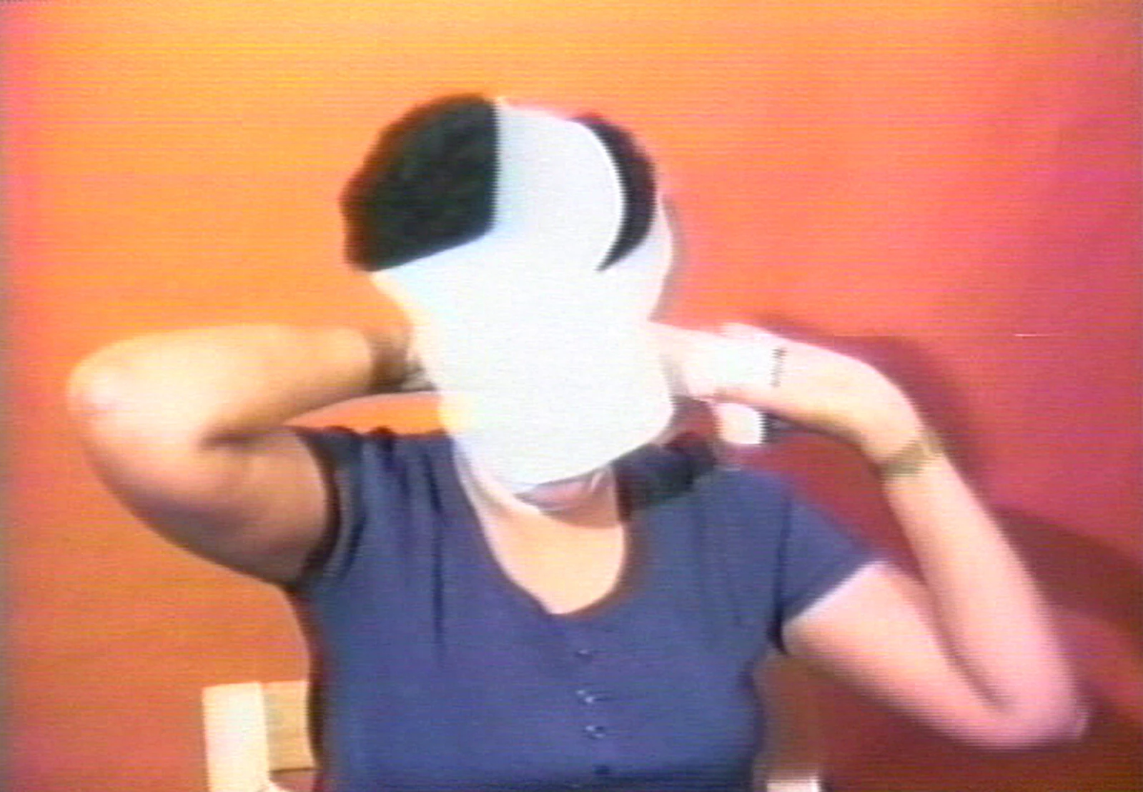 In this grainy image, a female-presenting person with a black afro is shown wrapping their face with a white bandage.