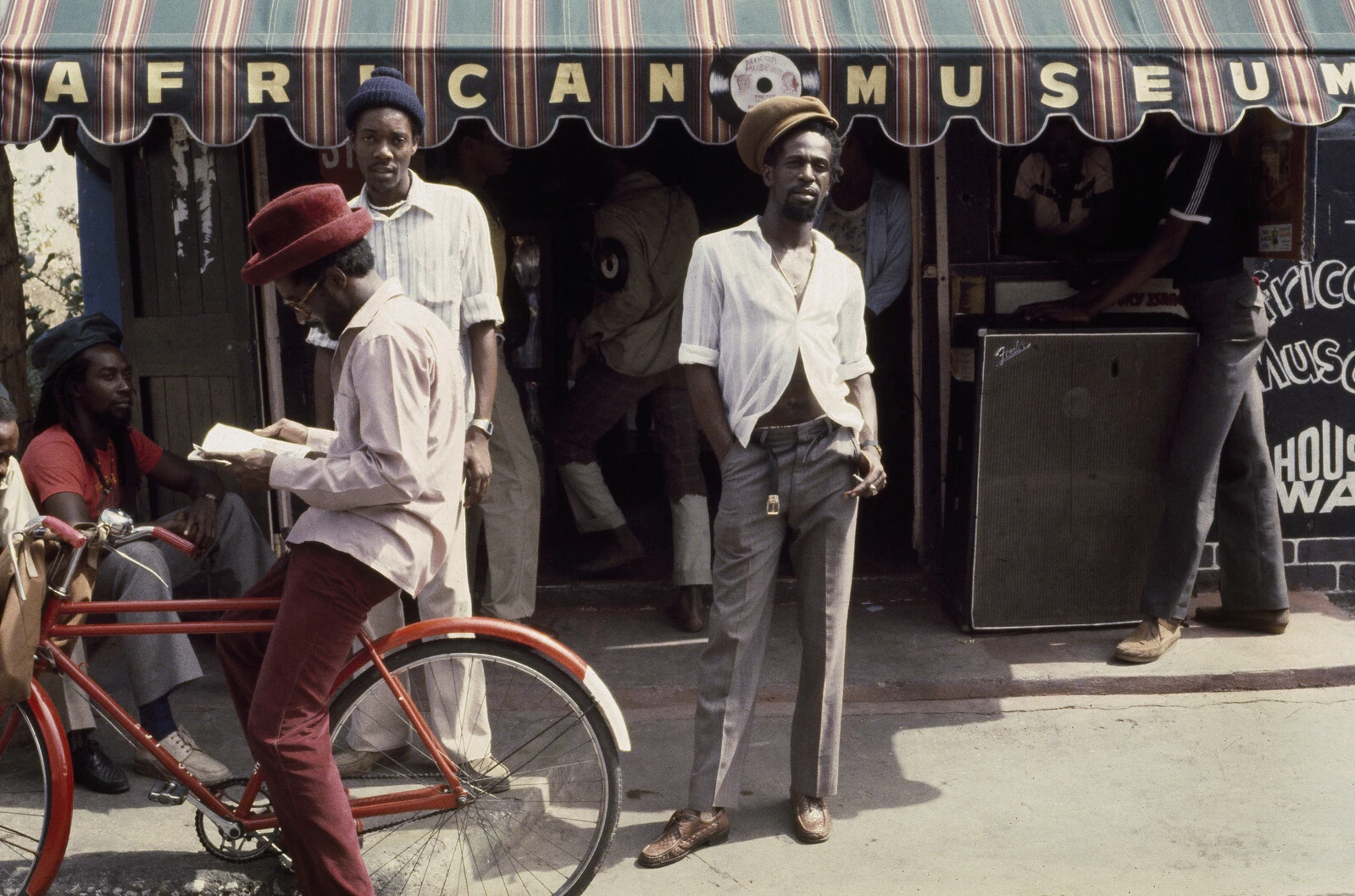 Archival photograph of a group of Black men standing in front of a shop with striped awning that has the name African Museum on it