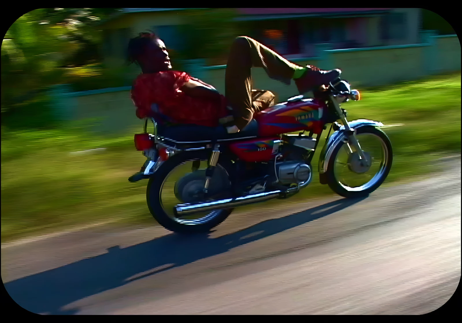 Blurry image of a person leaning back on a red motorcycle, their legs up on the handle bars, as the scenery blurs around them